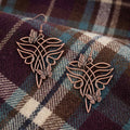 A pair of dangling earrings with a copper-toned metal design featuring a stylized leaf or wing shape and small butterfly details, displayed on a light textured surface.