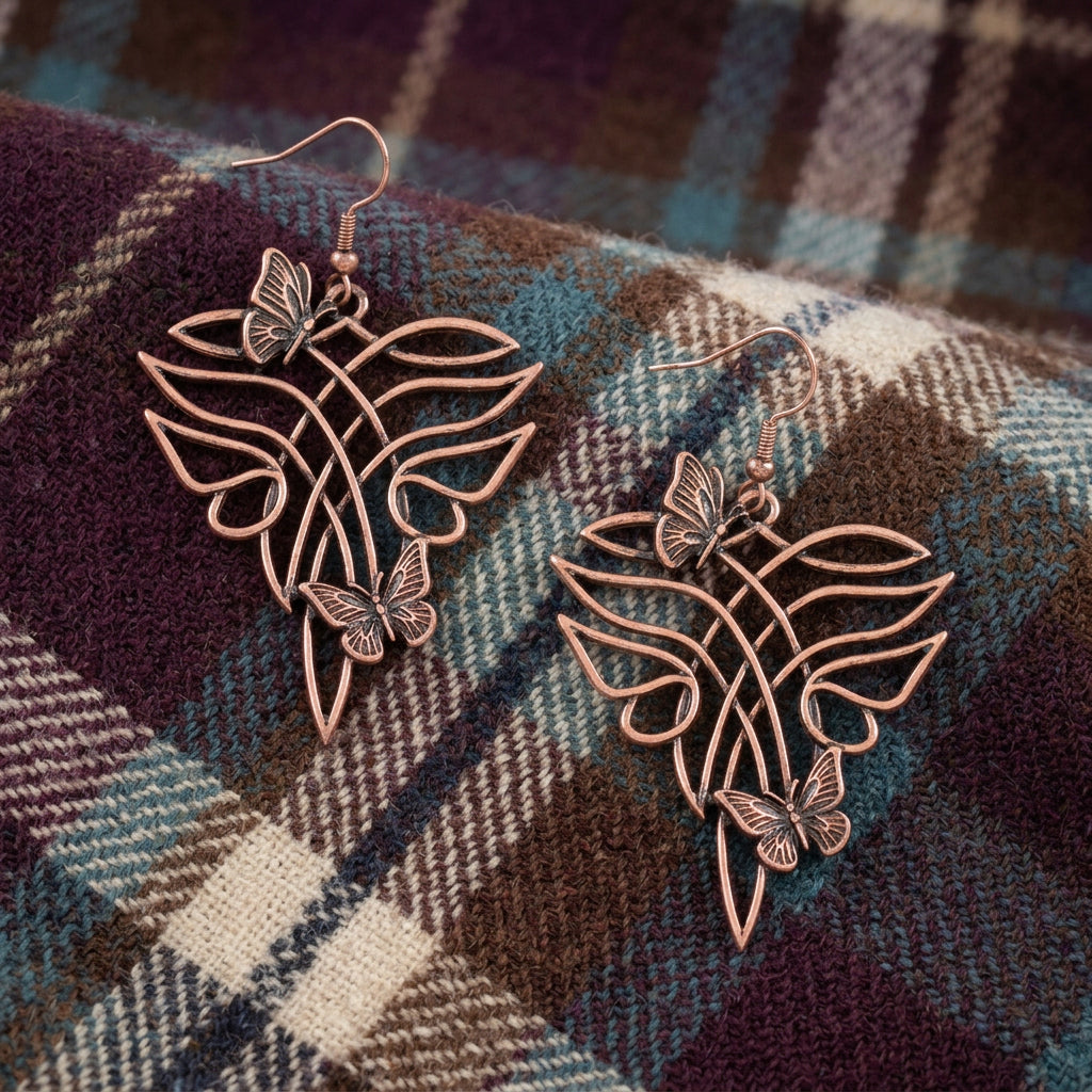 A pair of dangling earrings with a copper-toned metal design featuring a stylized leaf or wing shape and small butterfly details, displayed on a light textured surface.